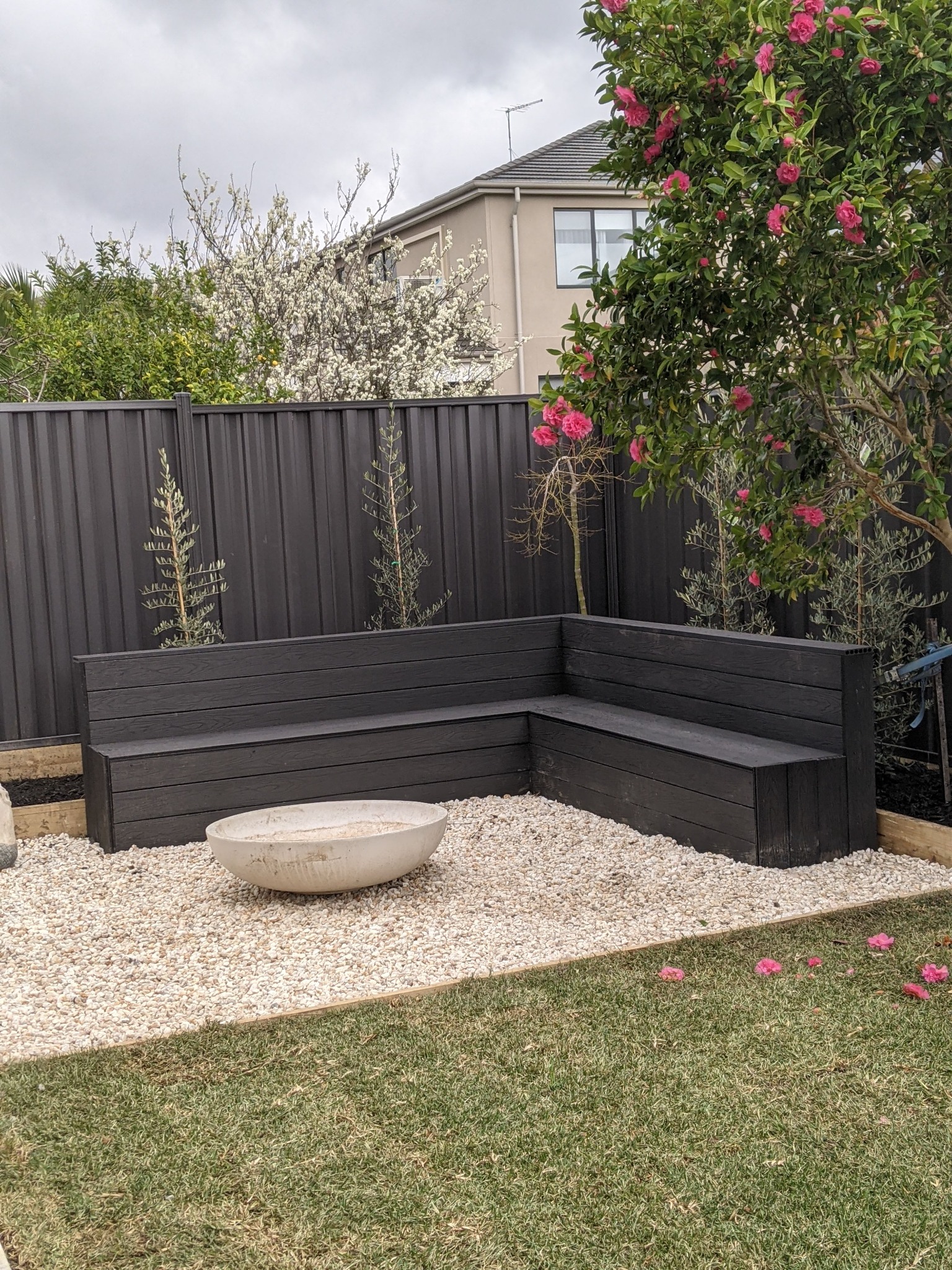 Custom black L-shaped built-in outdoor seating with planting and white pebbles
